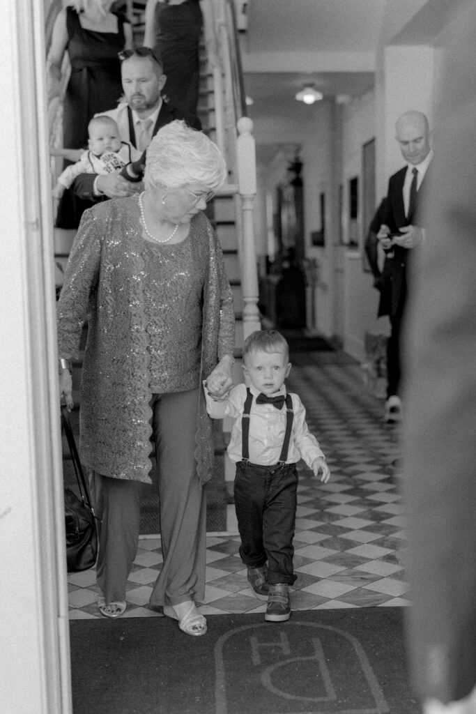 Young child in bowtie walks holding grandmother's hand. 