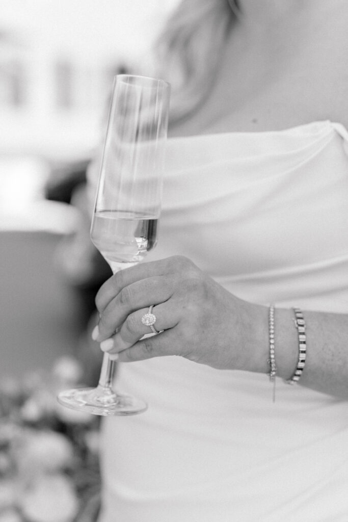 Black and white photo of bride holding glass of champagne with her wedding ring. 