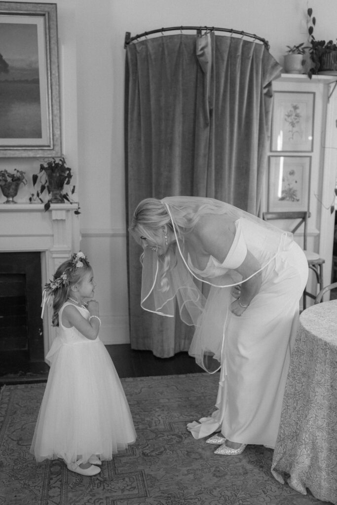 Black and white photo of bride bending down to talk to flower girl. 