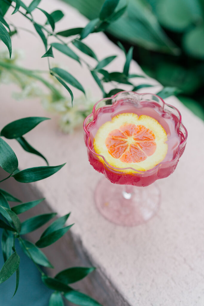 Clear pink cocktail glass with orange garnish.