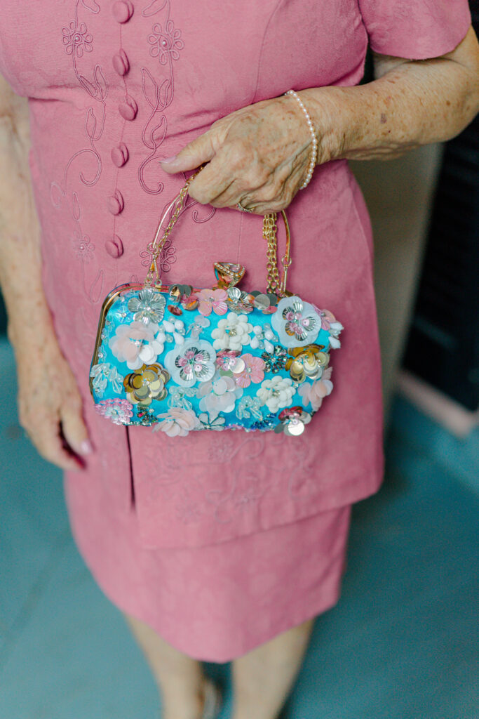 Grandmother of the bride wears pink outfit with fun blue statement purse. 