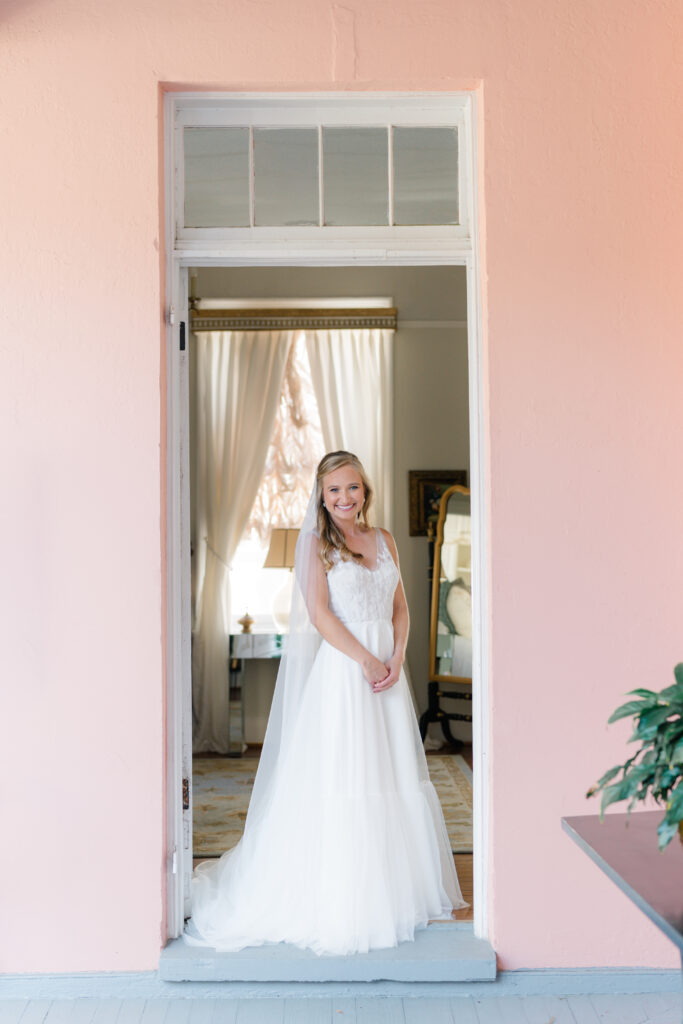 Bride poses for portrait in the doorway of pink house in Charleston.