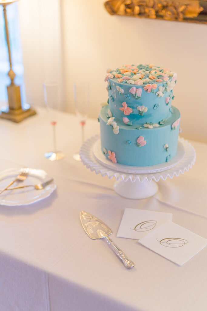 Two-tiered blue wedding cake with pink and white flower decoration. 