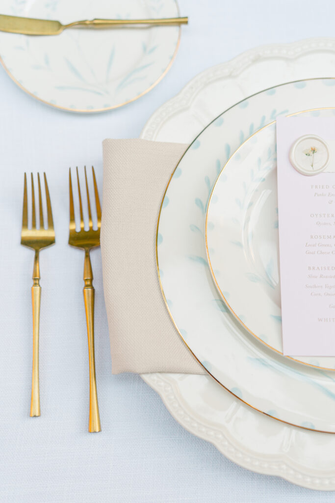 Gold utensils. Layered and textured place settings. Light cream with a touch of blue accents and pale pink menu. 