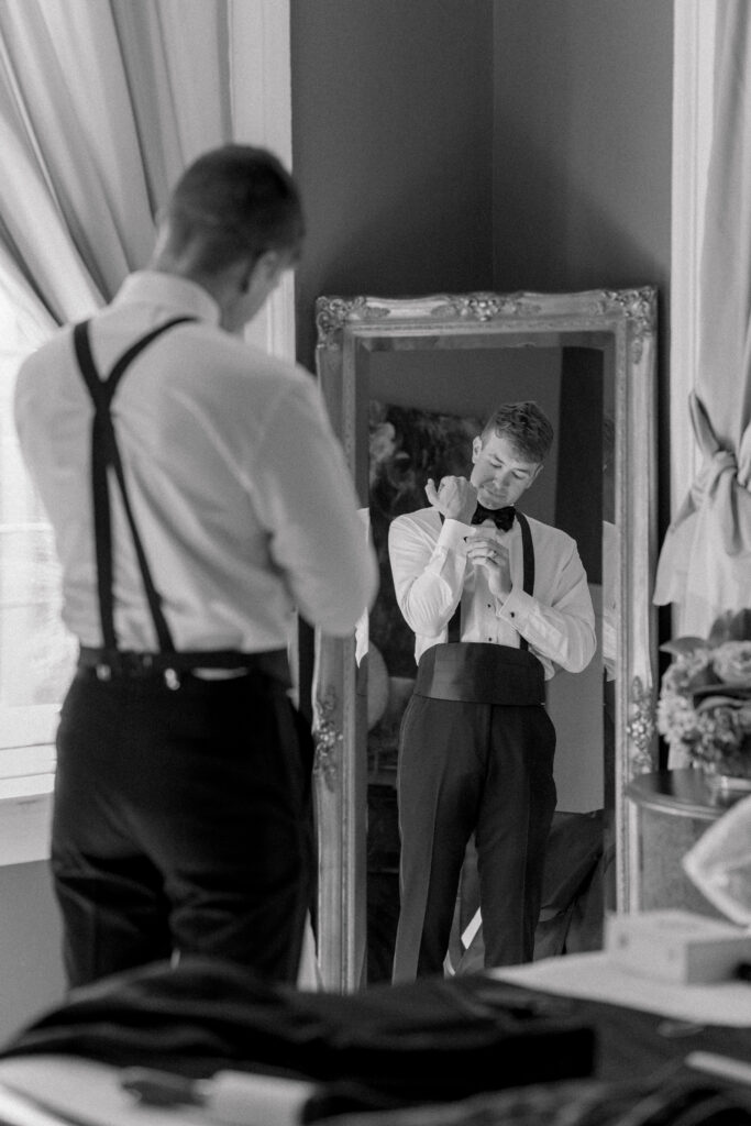 Groom puts on his cufflinks in the mirror. Black and white wedding photo. 