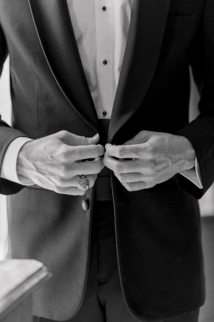 Black and white photo of grooms hands buttoning tuxedo jacket. 