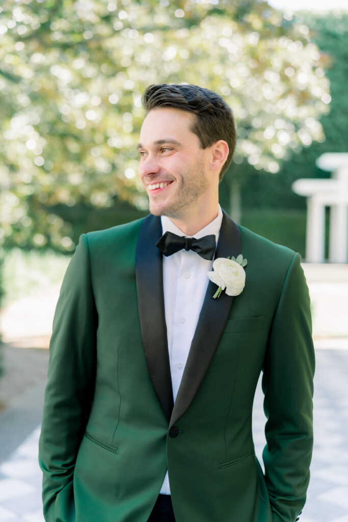 Groom in green tuxedo smiling and looking off to the side. 