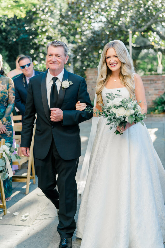 Father of the bride escorts daughter up aisle for outdoor wedding ceremony. 