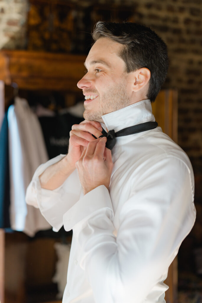 Groom fixes bowtie while getting ready on wedding day. 