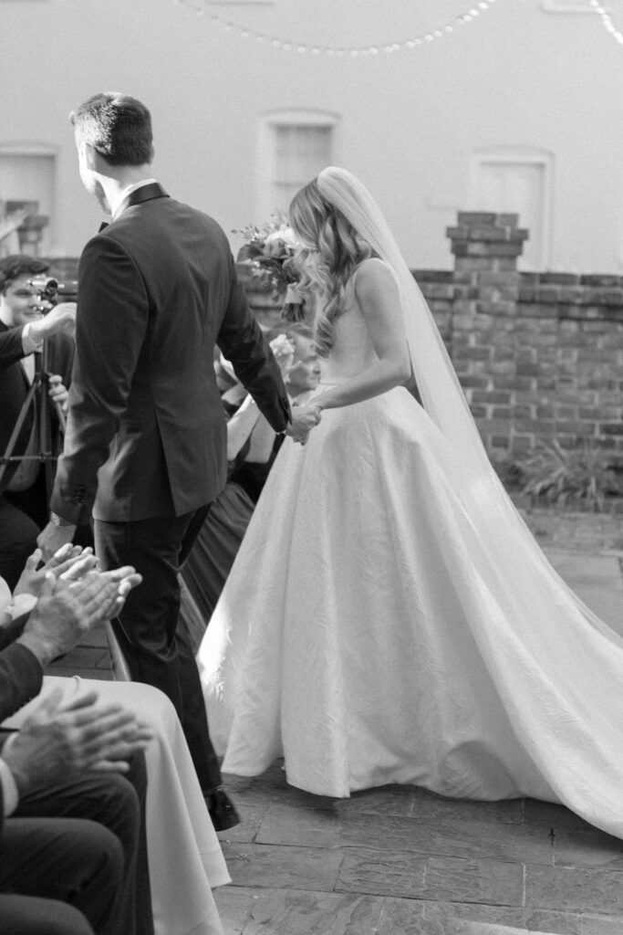 Groom leads bride down the aisle after outdoor wedding ceremony. 