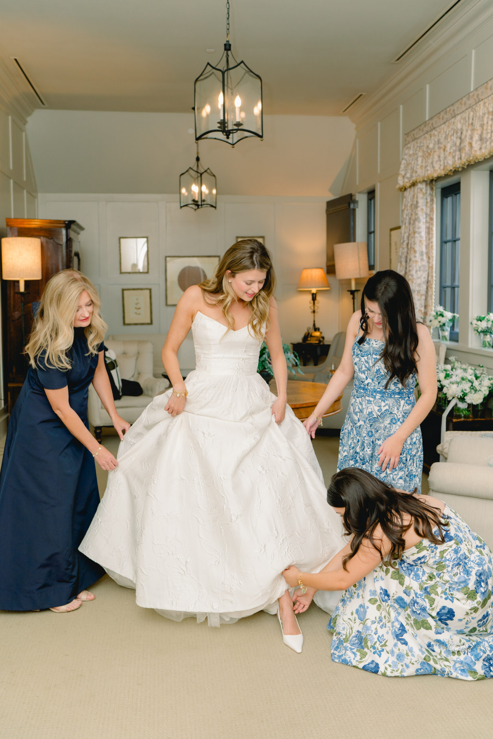 Sisters of the bride help her put on her heels on wedding day. 
