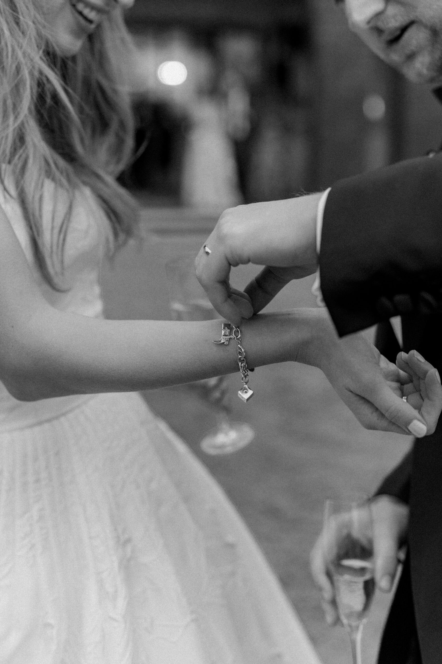 Groom helps bride adjust her charm bracelet. 