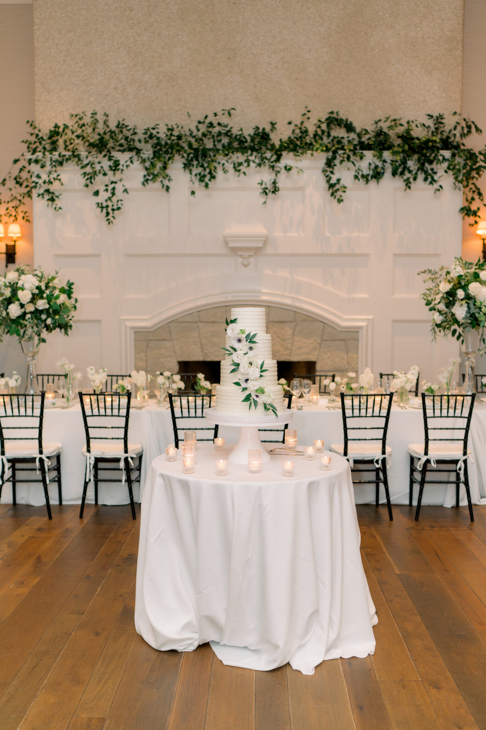 White and green wedding cake in front of the fireplace decorated in greenery. 