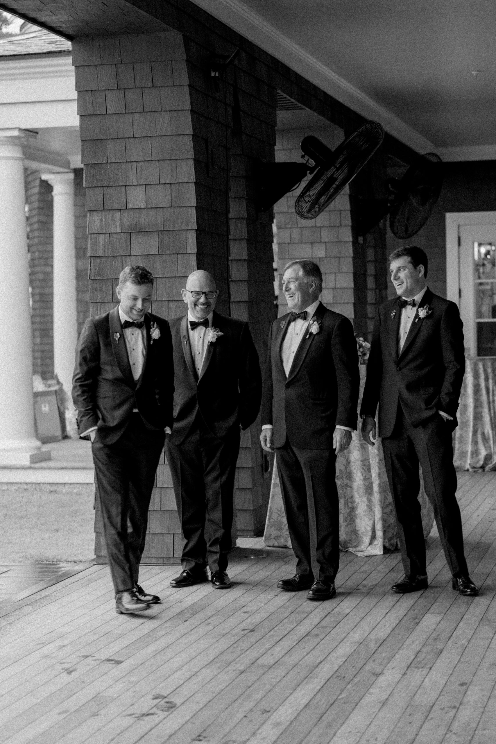 Groom on the porch with his dad, brother and father of the bride. Candid black and white wedding photo. 