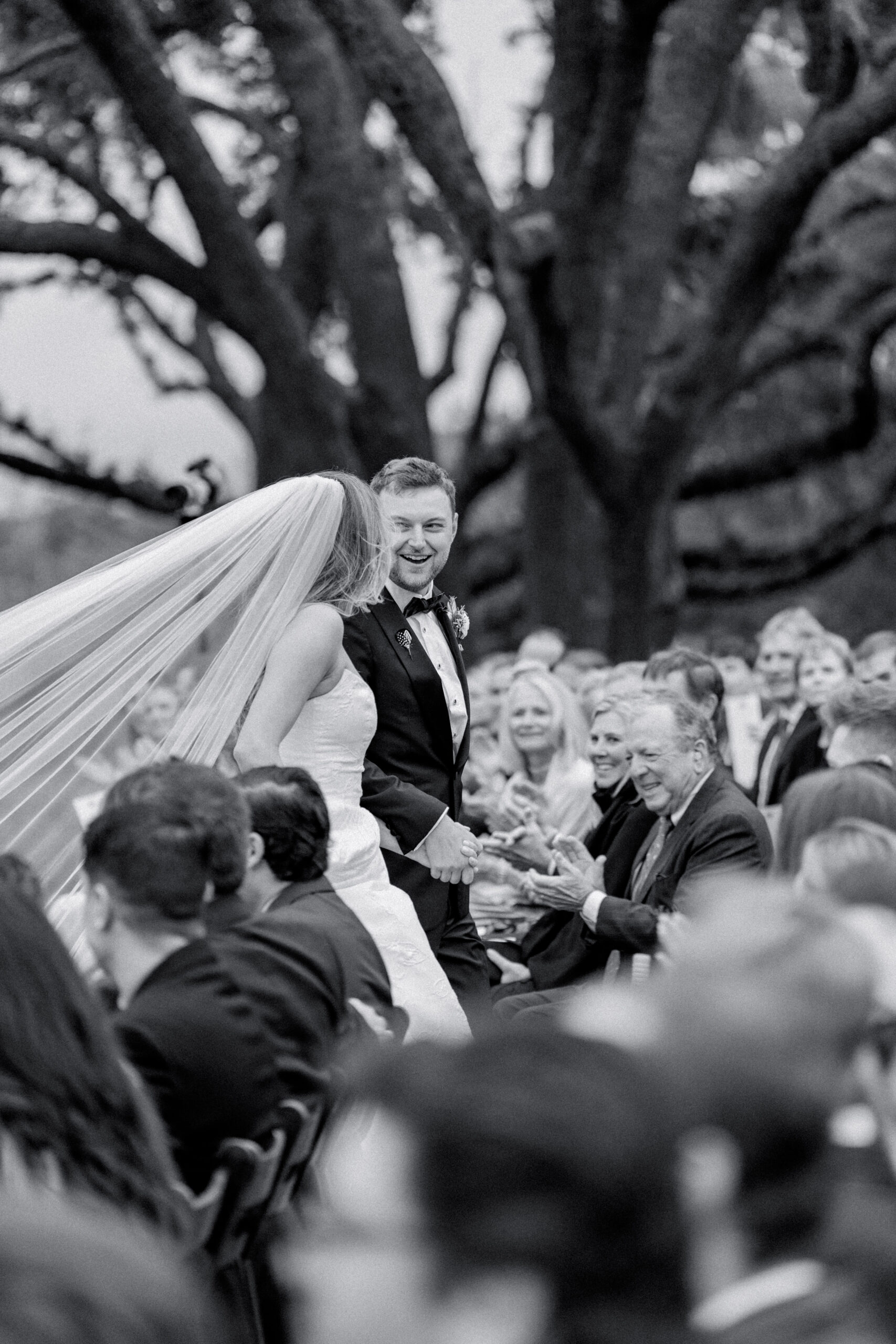 Black and white wedding photo. Wedding guests clap as bride and groom exit ceremony. Charleston weddings. 