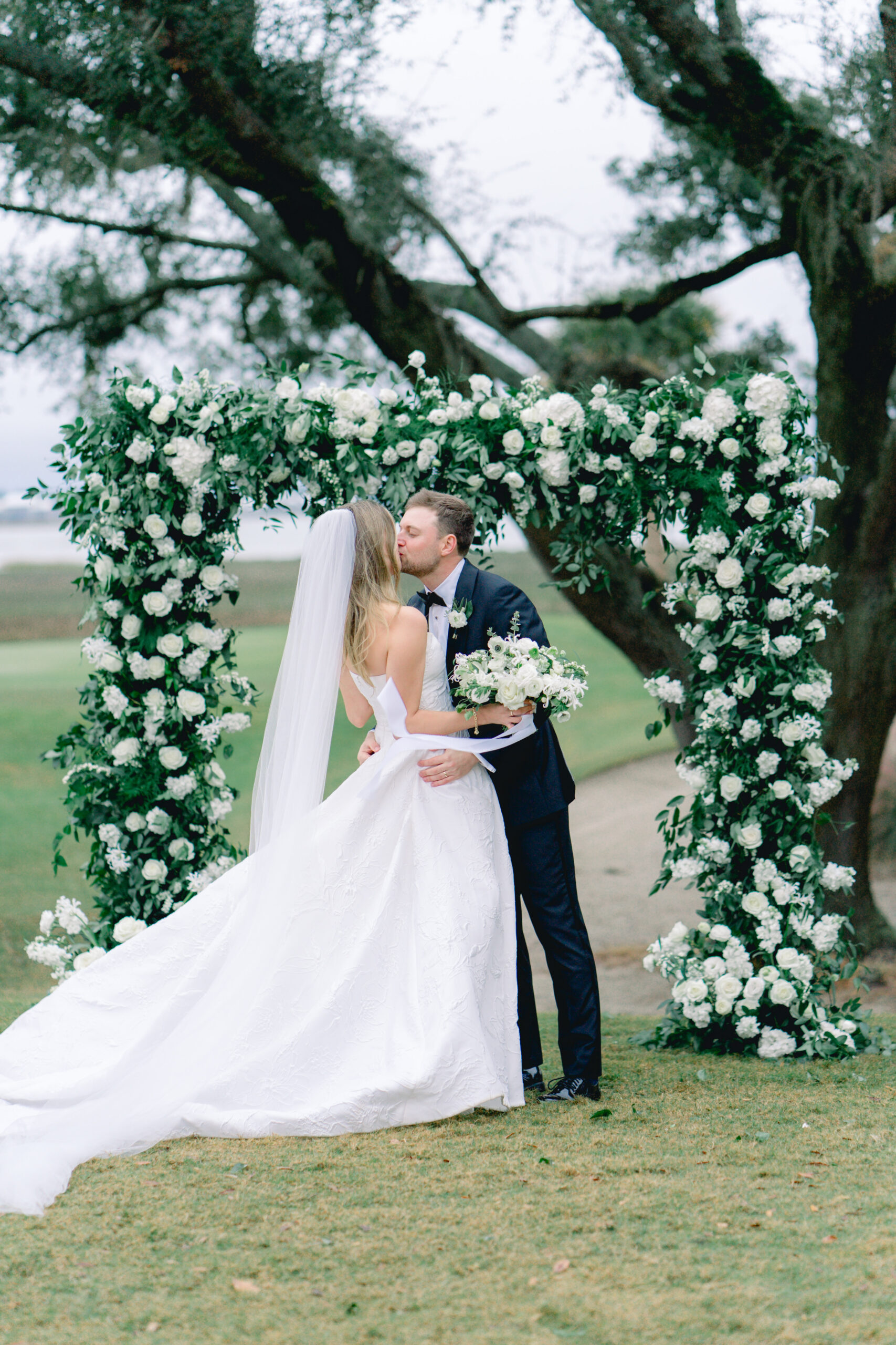 Bride and groom kissing in front of floral arch. Kiawah River Course wedding. 