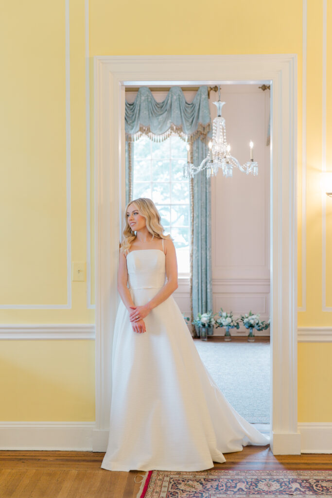 Bride standing in the doorway with yellow walls. Wedding dress at Lowndes Grove. 