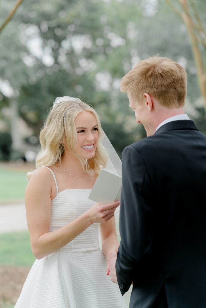Bride smiles at groom during vow reading at Lowndes Grove winter wedding.