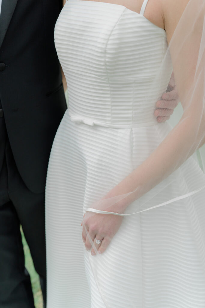 Detail photo of bride holding her veil with wedding ring and groom's hand. 