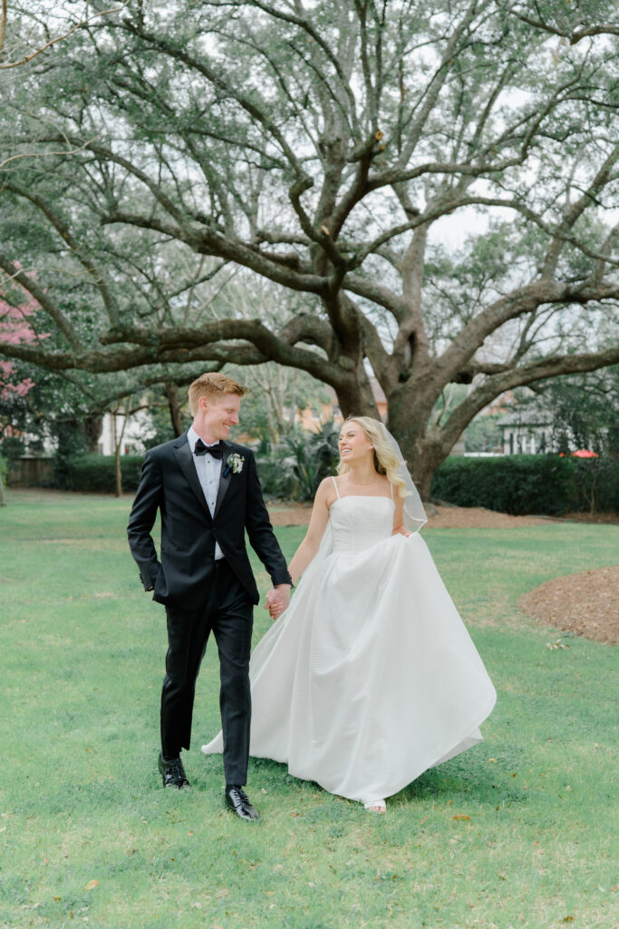 Bride and groom walking with live oak tree in the background. Winter wedding in Charleston. 