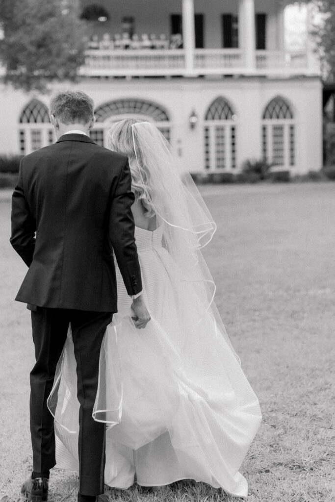 Black and white candid photo of groom helping bride walk with her dress.