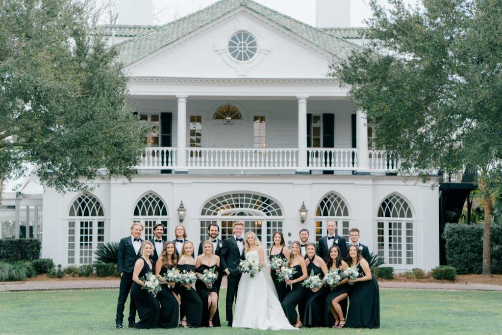 Symmetrical group photo of full bridal party standing in front of Lowndes Grove. Winter destination wedding in Charleston. 