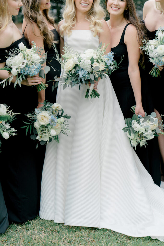 Bridesmaids in black with white flowers and touches of pastel blue. 