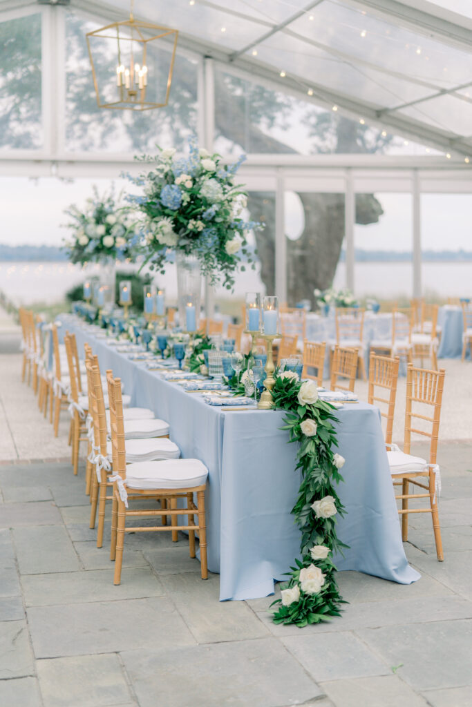 Head table at Lowndes Grove lined with greenery and white flowers. Blue linen table cloth. 
