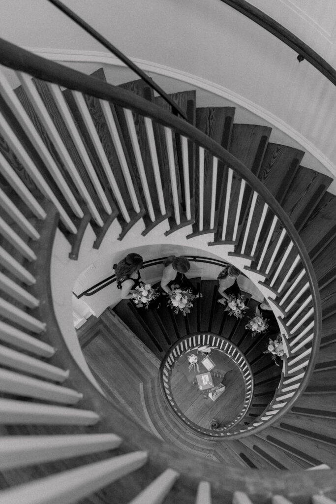 Black and white photo of bridesmaids walking down curved staircase at Lowndes Grove. 