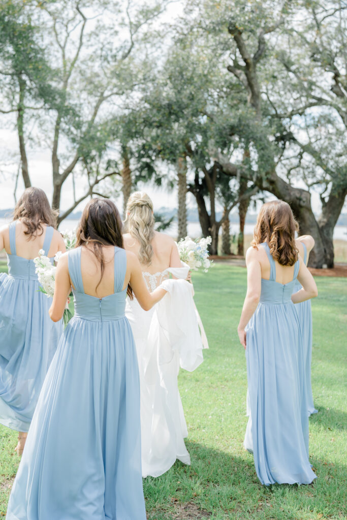 Bridesmaids helping bride with dress walking on the lawn. 