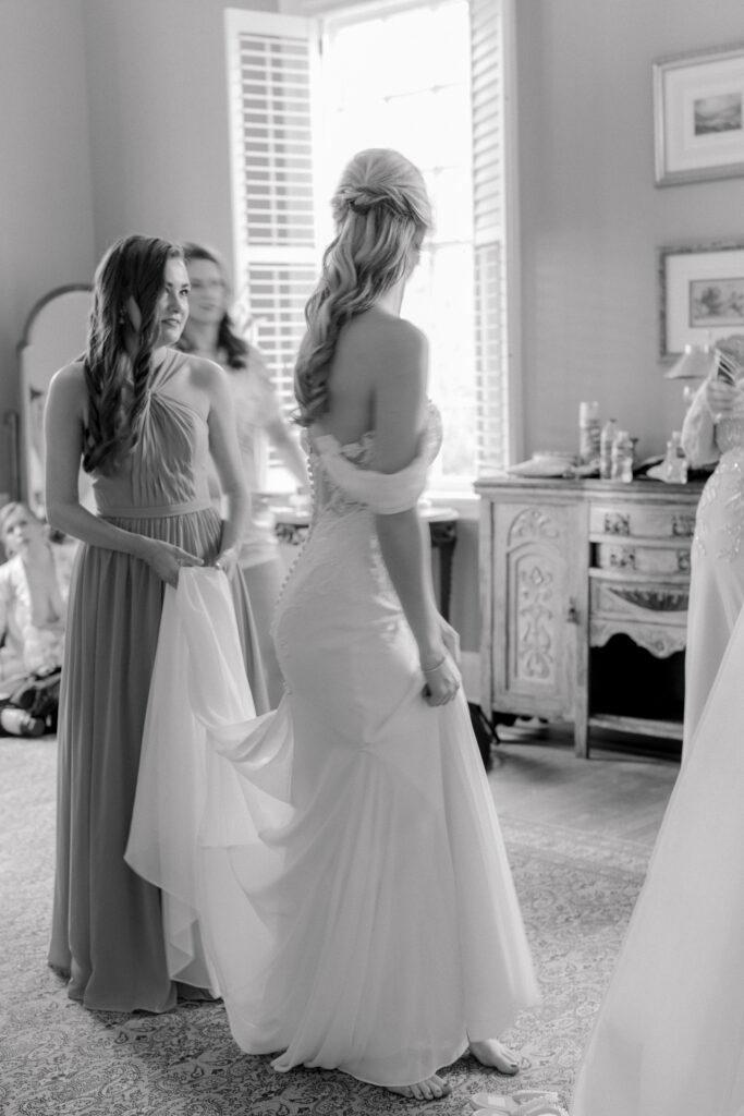 Black and white photo of bridesmaids helping with wedding dress.