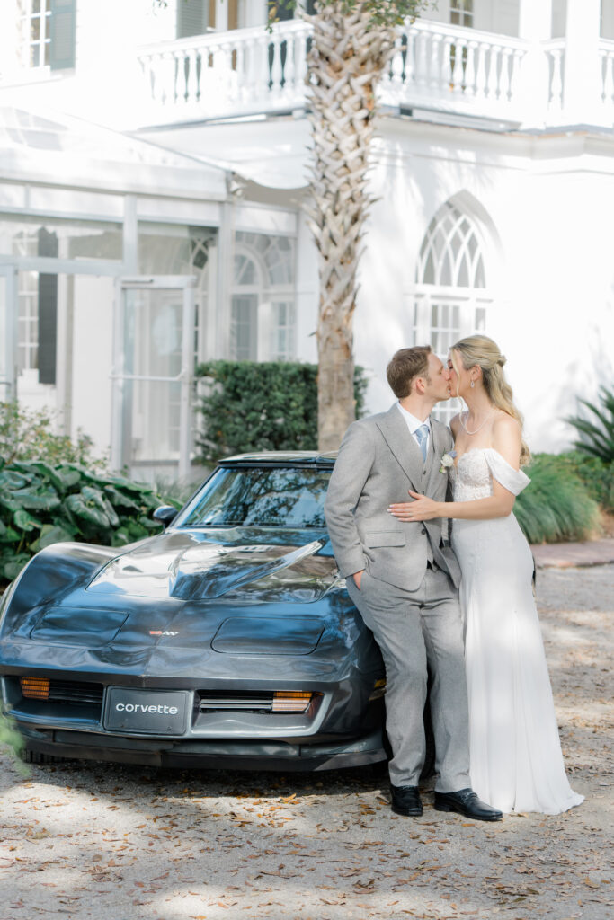 Bride and groom kiss while leaning on groom's corvette. 