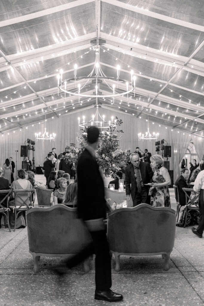 Blurry black and white guest photo of dinner time at Lowndes Grove wedding. String lights and hanging modern circular chandeliers. 