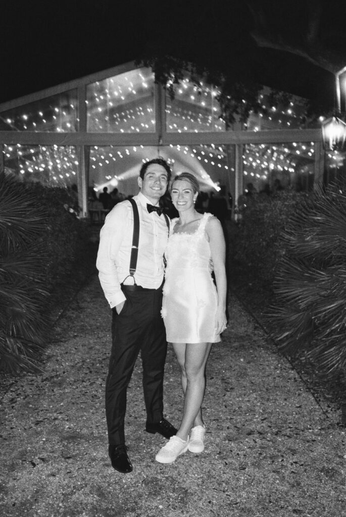 Flash film photo of bride and groom with tent and string lights in background.
