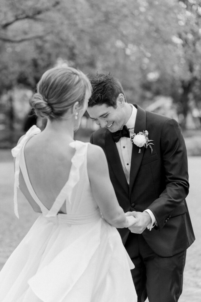 Candid black and white photo of groom smiling during first look with bride.