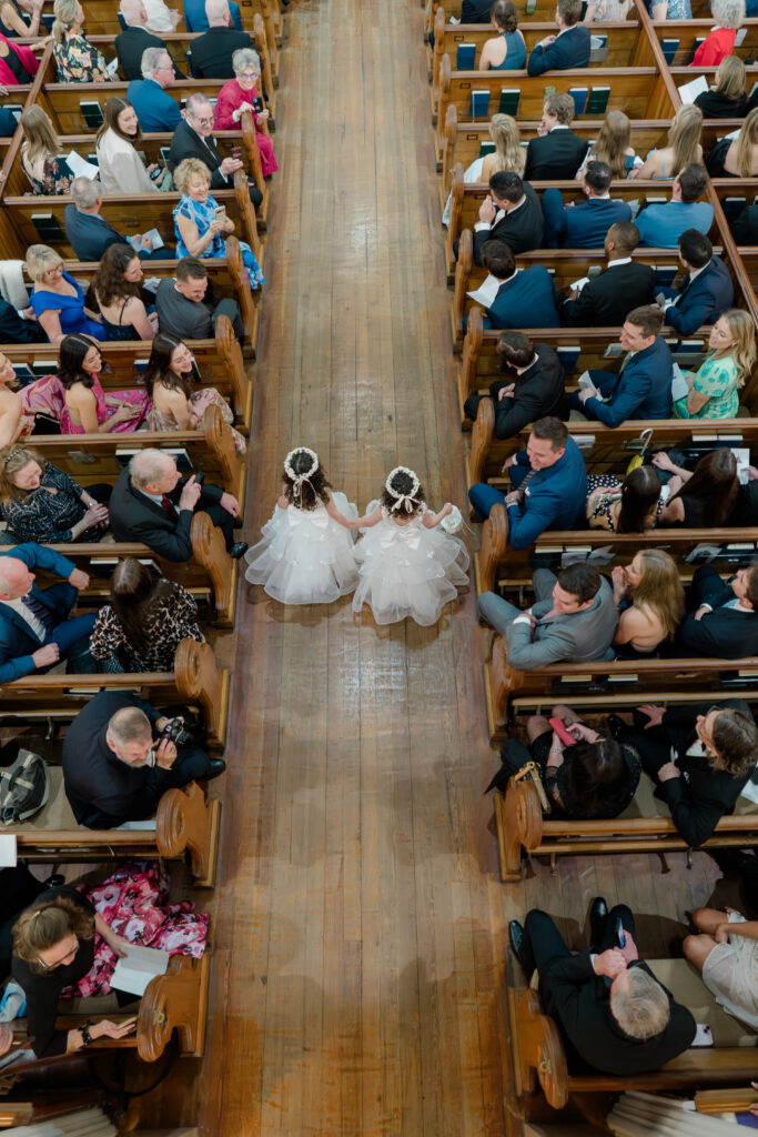 Bridesmaids hold hands and walk up the aisle with wedding guests watching. charleston church wedding ceremony. 
