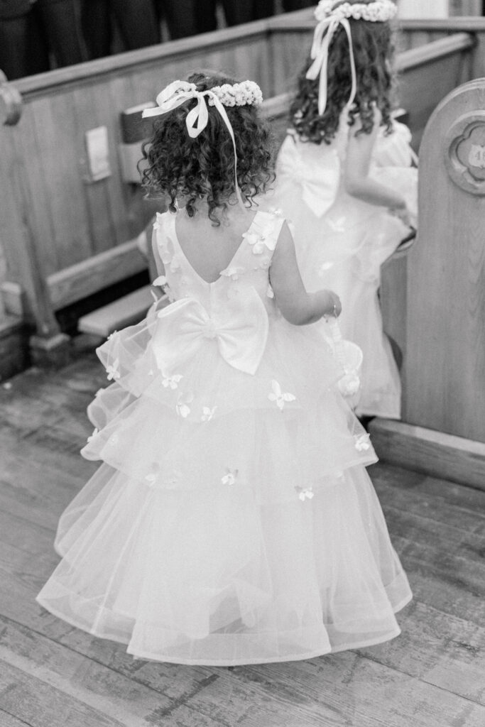 Black and white photo of flower girls at wedding ceremony. Cute flower crowns and long dresses with bow on the back. 