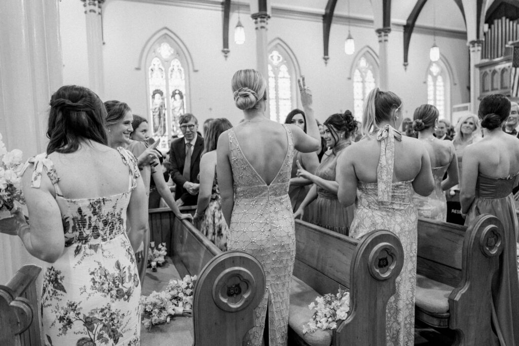Black and white candid photo of bridesmaids at church wedding ceremony. 