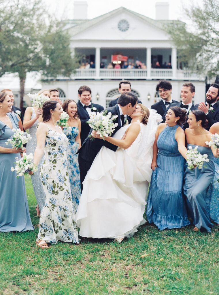 Groom dips back bride for a kiss with full bridal party celebrating.