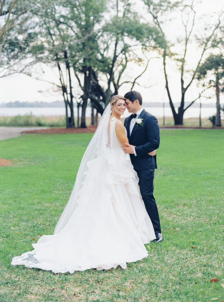 Bride and groom film photo. Green grass and trees with river in background. Waterfront spring wedding.