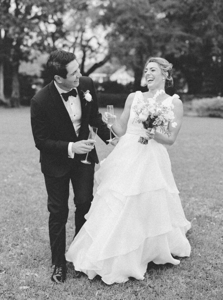 Black and white candid photo of bride and groom laughing with champagne. 