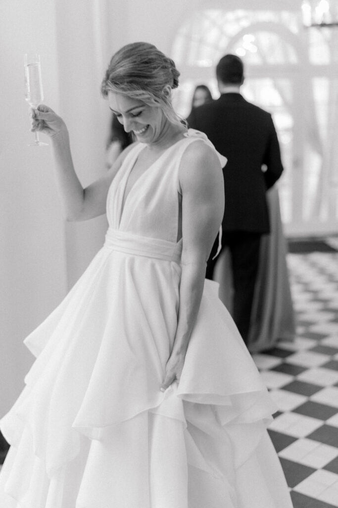 Candid black and white photo of bride laughing with champagne glass during cocktail hour. Spring wedding in Charleston, SC.