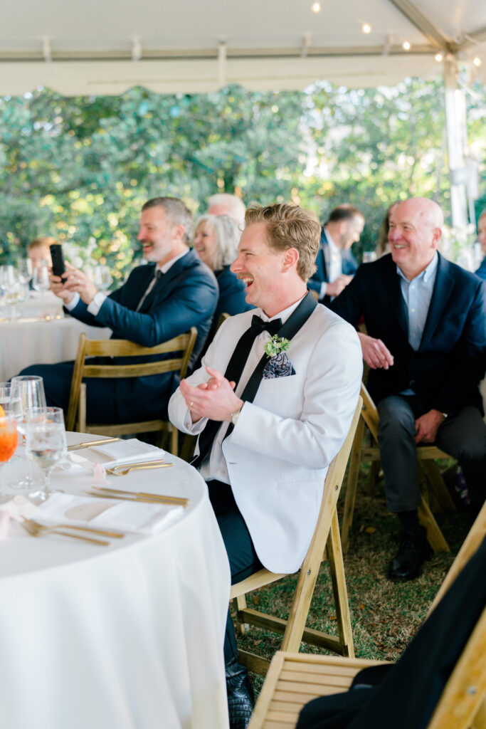 Groom laughs and claps at River House at Lowndes Grove wedding reception. 