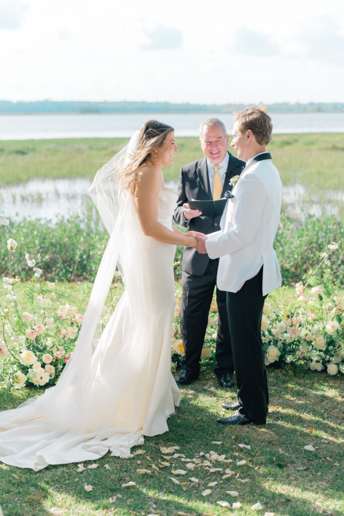 Riverfront wedding ceremony vows. Charleston spring wedding. Groom in white tux jacket. 