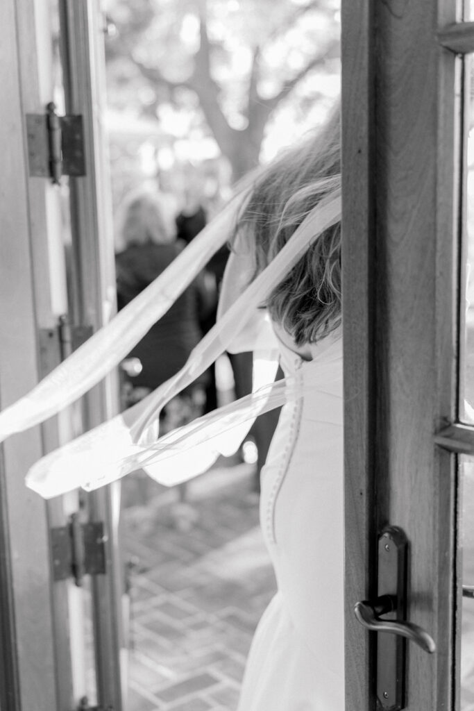 Bride's wispy lace dress blowing in the wind as she exits through a door. 