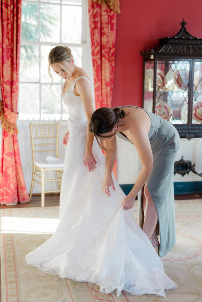Maid of honor helps the bride bustle her wedding dress in the red room at William Aiken House. 
