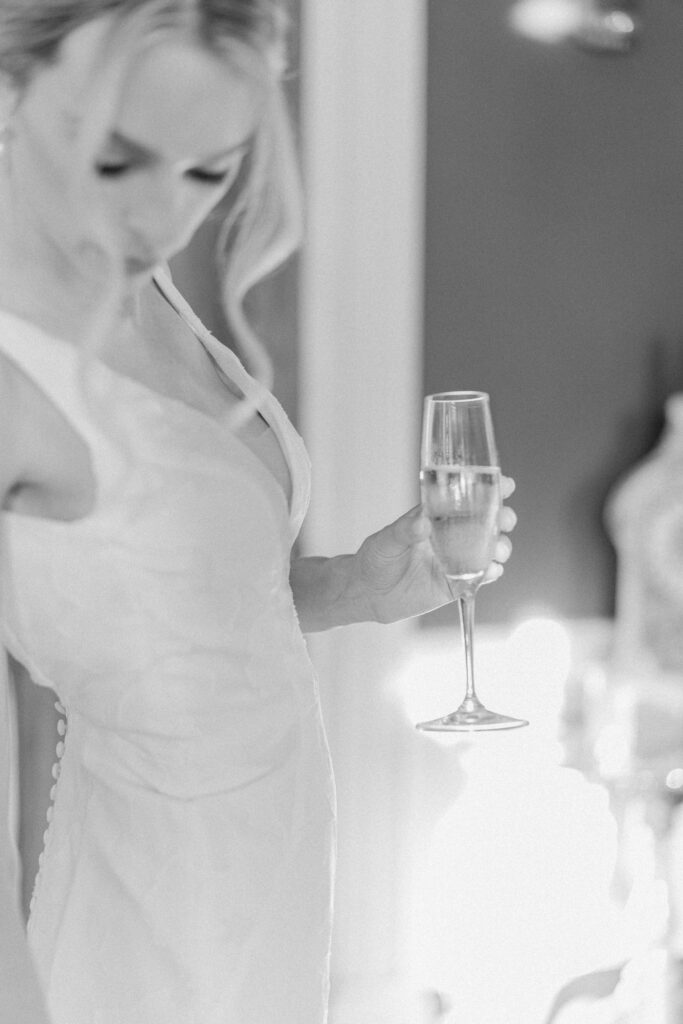 Black and white photo of bride holding champagne glass on wedding day. Charleston wedding photographer. 