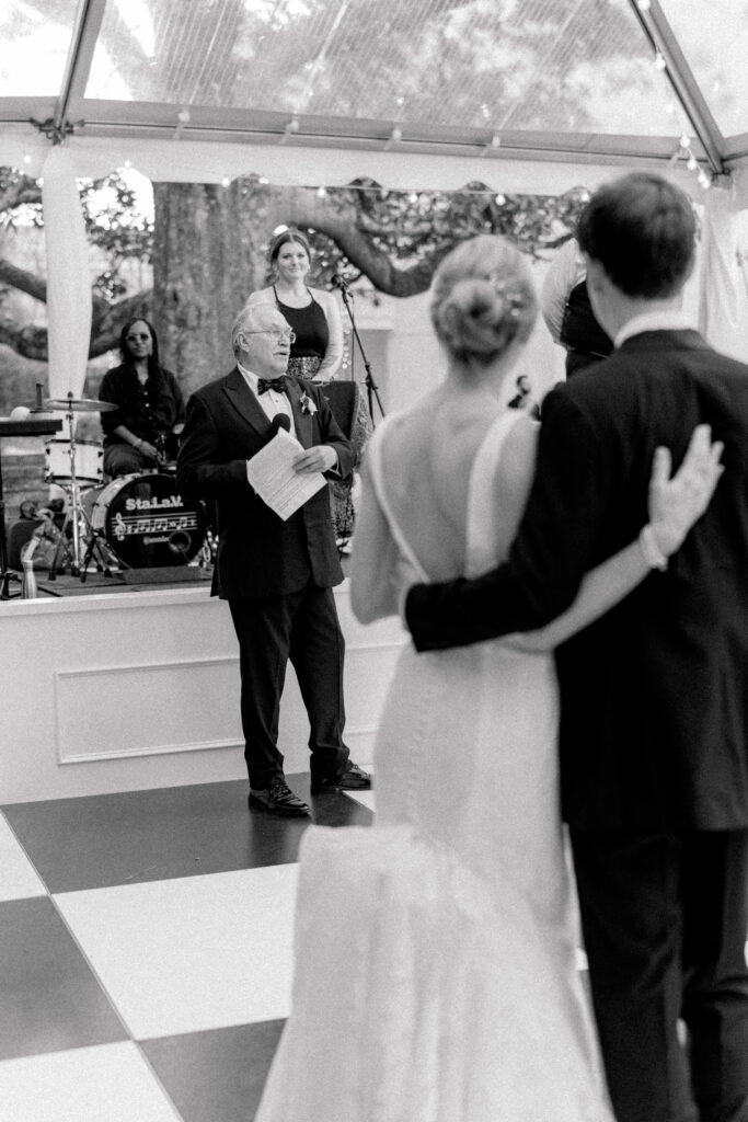 Grandfather of the bride gives welcome speech with bride and groom standing arm-in-arm.