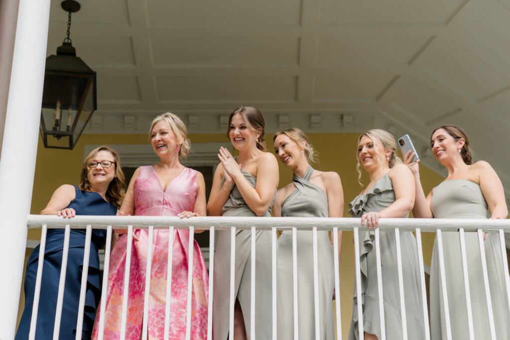 Mothers of the bride and groom and bridesmaids watch the first look from the porch at William Aiken House.