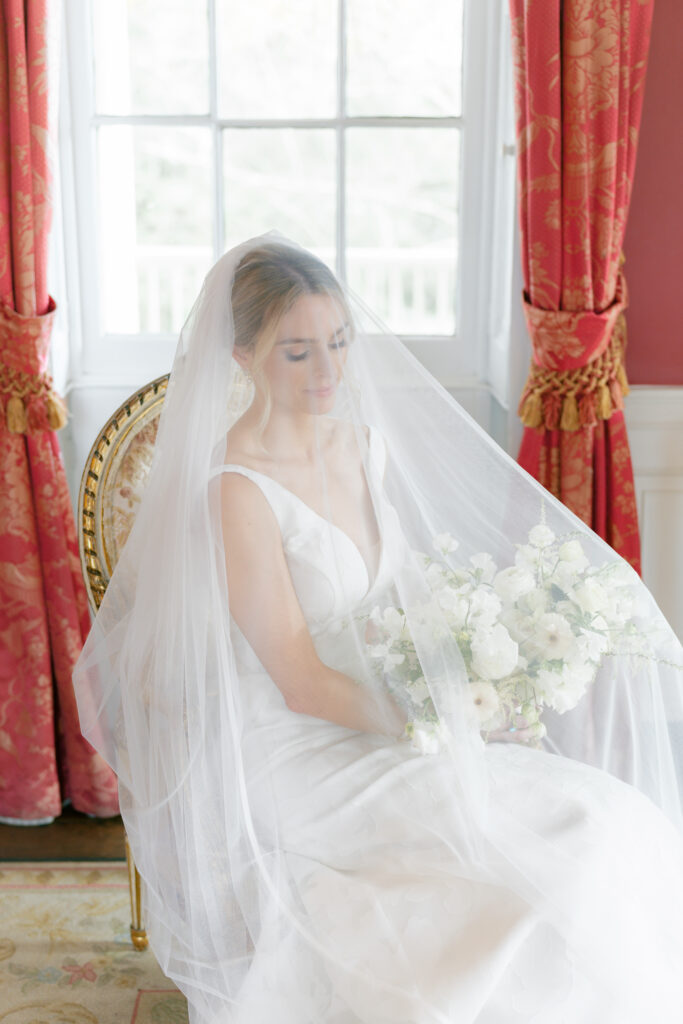 Bride covered in veil sitting in a chair in the red room at William Aiken House. 